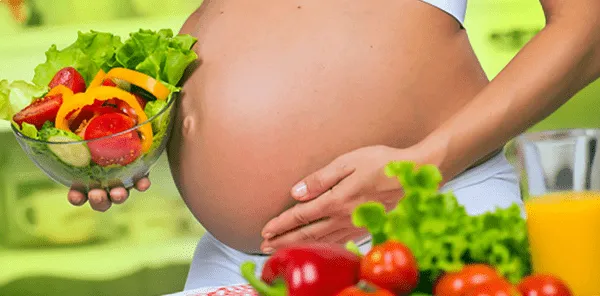 Schwangere Frau hält eine Schüssel Gemüsesalat in der Hand und legt Wert auf gesunde Ernährung.
